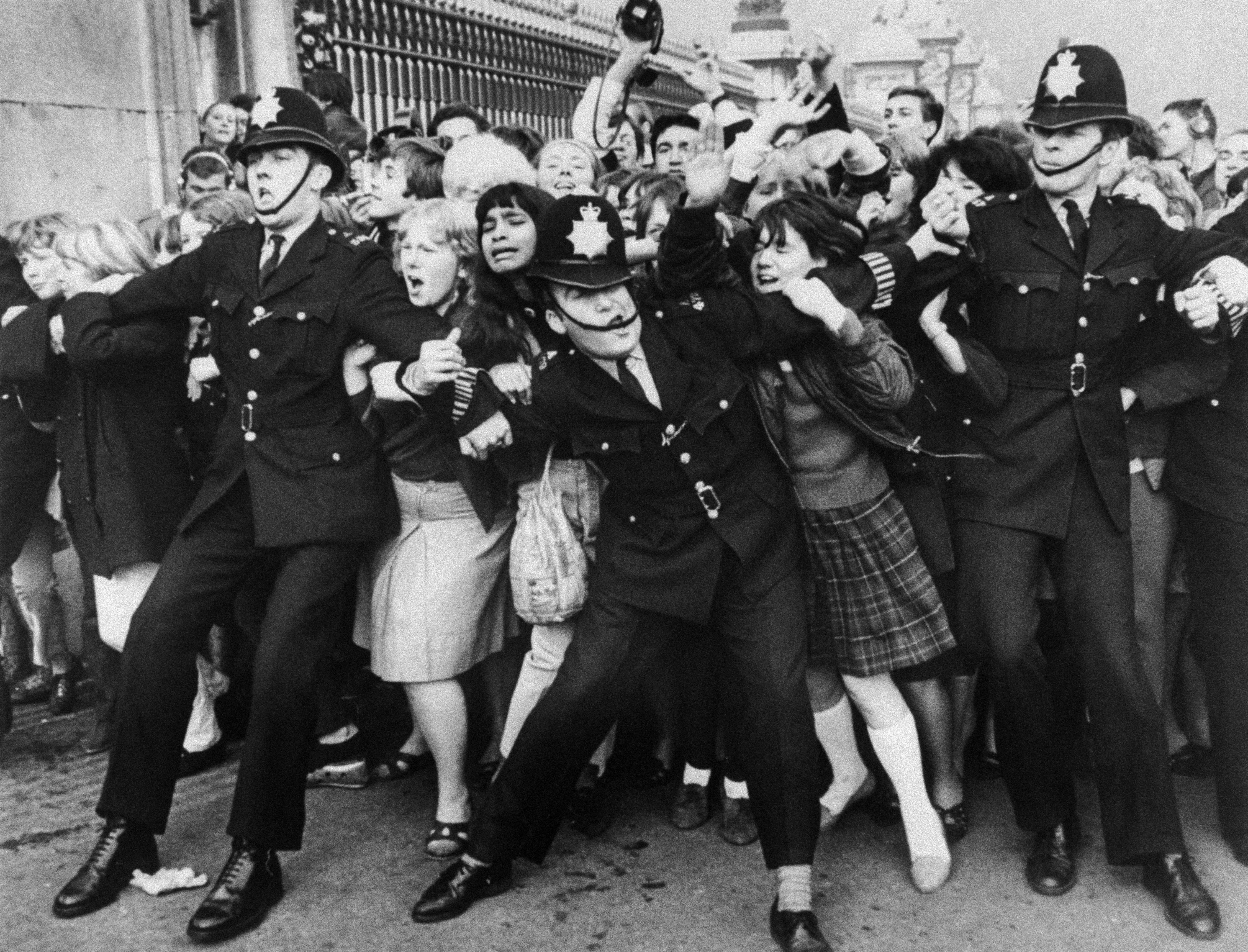 แฟนคลับที่รอต้อนรับสี่เต่าทอง ขณะที่วงเข้าเฝ้าสมเด็จพระราชินีนาถ Elizabeth II ณ พระราชวัง Buckingham เมื่อปี 1965 สะท้อนถึงปรากฏการณ์ Beatlemania ในยุคนั้น (ภาพ: Central Press/AFP)