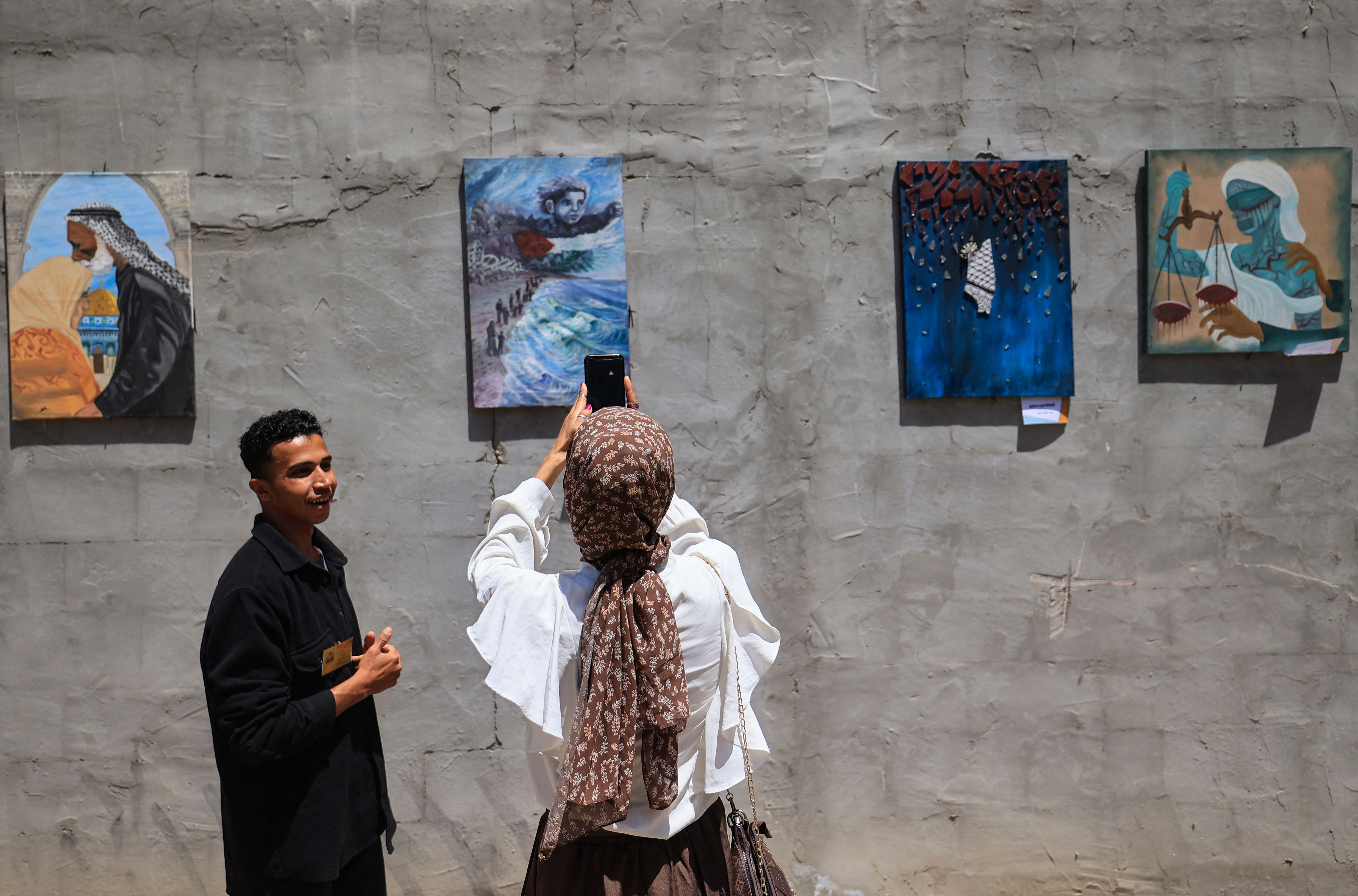 ผู้เยี่ยมชมคนหนึ่งกำลังถ่ายภาพวาดที่มีธงปาเลสไตน์เป็นองค์ประกอบหลัก (ภาพ: Eyad Baba/AFP)